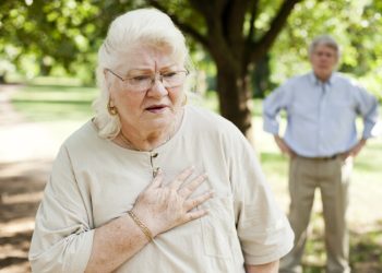 A senior woman experiencing chest pain.  A senior man is in the background.