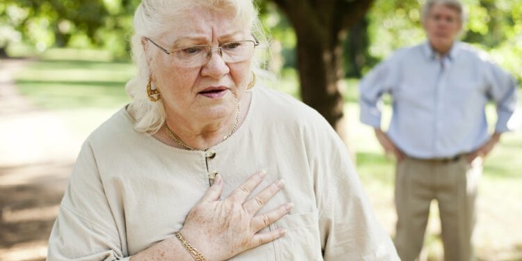 A senior woman experiencing chest pain.  A senior man is in the background.