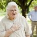 A senior woman experiencing chest pain.  A senior man is in the background.